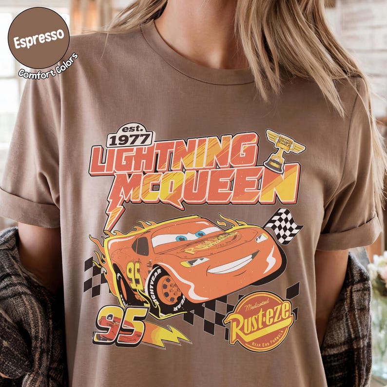Op de afbeelding: Espresso-kleurig T-shirt met een afbeelding van Lightning McQueen uit de film Cars. Het ontwerp bevat de tekst "Lightning McQueen" en "95", samen met een geblokte vlag en een trofee. Het shirt is gemaakt van een zacht, comfortabel materiaal.