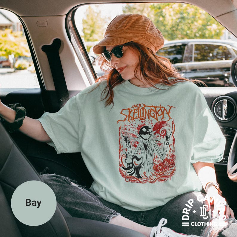 Puede incluir: Camiseta verde claro con un dise&ntilde;o rojo y negro de Jack Skellington. El dise&ntilde;o incluye el texto "Jack Skellington". La camiseta es parte de una colecci&oacute;n de ropa. La persona lleva un sombrero marr&oacute;n y gafas de sol.