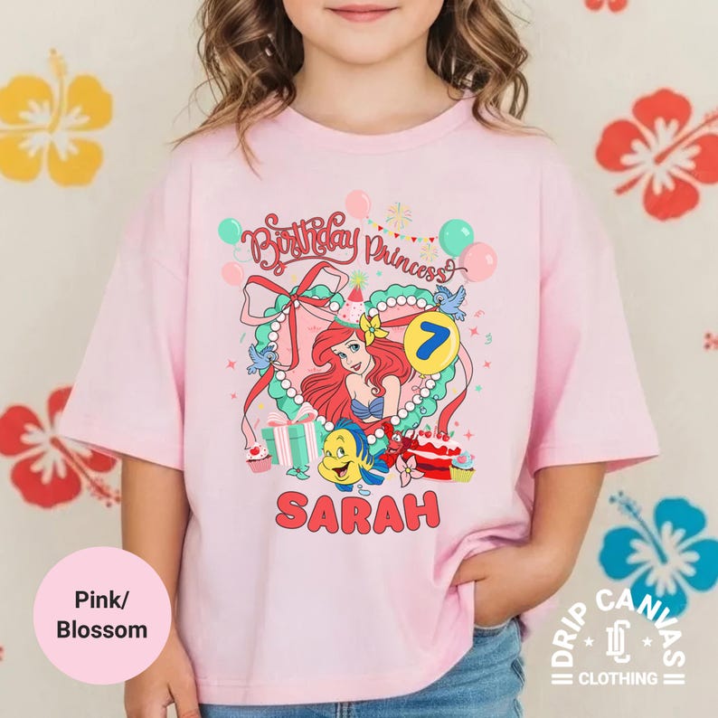 May include: Pink t-shirt with a graphic featuring Ariel from The Little Mermaid, the text "Birthday Princess", the number 7, and the name "Sarah". The shirt has a round neck and short sleeves. The shirt is labeled "Pink/Blossom".