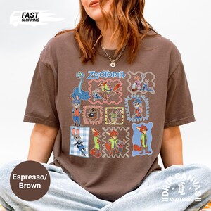 May include: Espresso brown t-shirt featuring a colorful Zootopia graphic. The design includes various characters in framed illustrations. The shirt has a relaxed fit and is made of a soft material. The words "Zootopia" are at the top of the design.