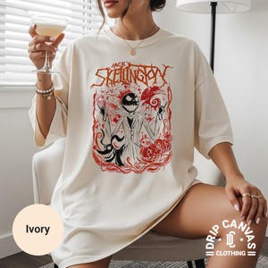 Puede incluir: Camiseta de color marfil con un gr&aacute;fico de Jack Skellington de The Nightmare Before Christmas. El dise&ntilde;o incluye detalles en rojo y el texto "Jack Skellington". La camiseta forma parte de la colecci&oacute;n Drip Canvas Clothing.
