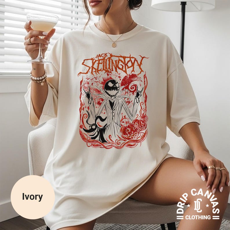 Puede incluir: Camiseta de color marfil con un gr&aacute;fico de Jack Skellington de The Nightmare Before Christmas. El dise&ntilde;o incluye detalles en rojo y el texto "Jack Skellington". La camiseta forma parte de la colecci&oacute;n Drip Canvas Clothing.