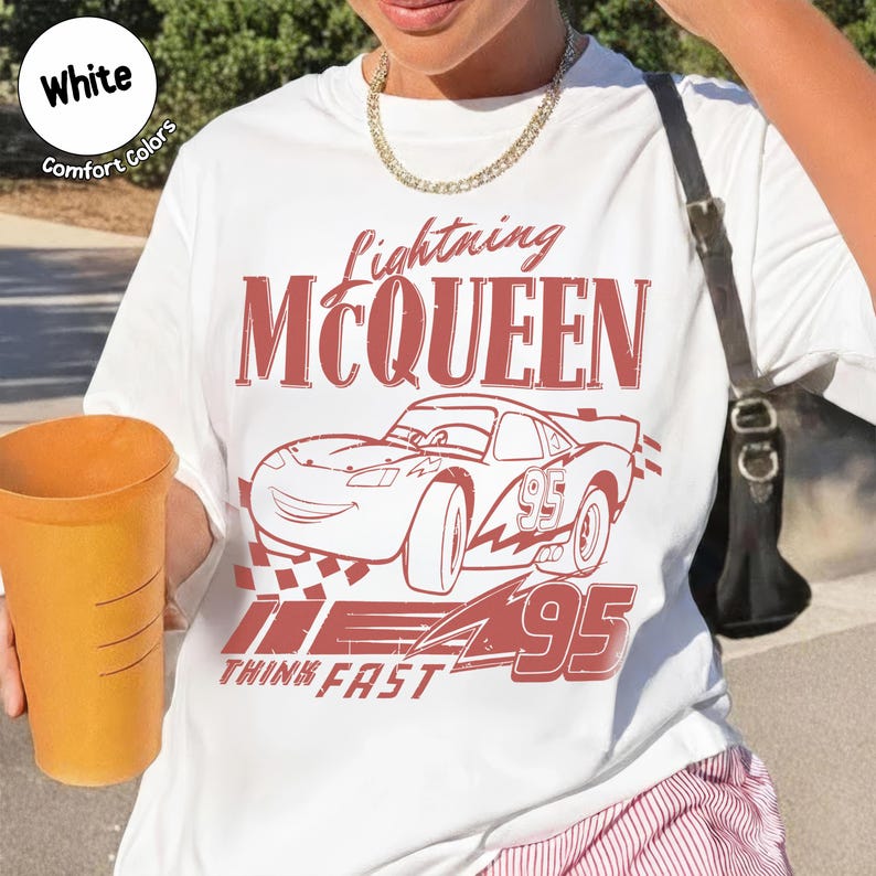 K&ouml;nnte beinhalten: Wei&szlig;es T-Shirt mit einem roten Aufdruck von Lightning McQueen aus dem Film Cars. Das Design umfasst den Namen der Figur, eine Rennwagen-Illustration und die Nummer 95. Die Worte "Think Fast" sind ebenfalls auf dem T-Shirt aufgedruckt.
