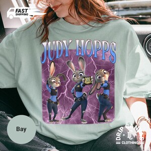 May include: Light green t-shirt featuring the text "JUDY HOPPS" above a graphic of three cartoon bunnies in police uniforms. The graphic has a purple background with lightning bolts.