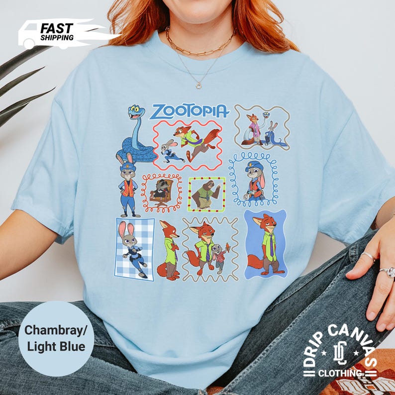May include: Light blue t-shirt featuring multiple framed illustrations of characters from the animated film "Zootopia." The shirt includes the film's title and the words "Chambray/Light Blue."