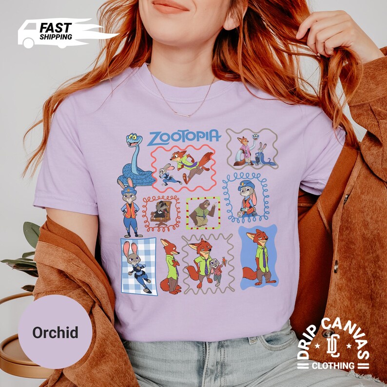 May include: A light purple t-shirt featuring a colorful graphic of characters from the movie "Zootopia". The design includes various framed illustrations of the characters. The shirt also has the word "Zootopia" printed on it.