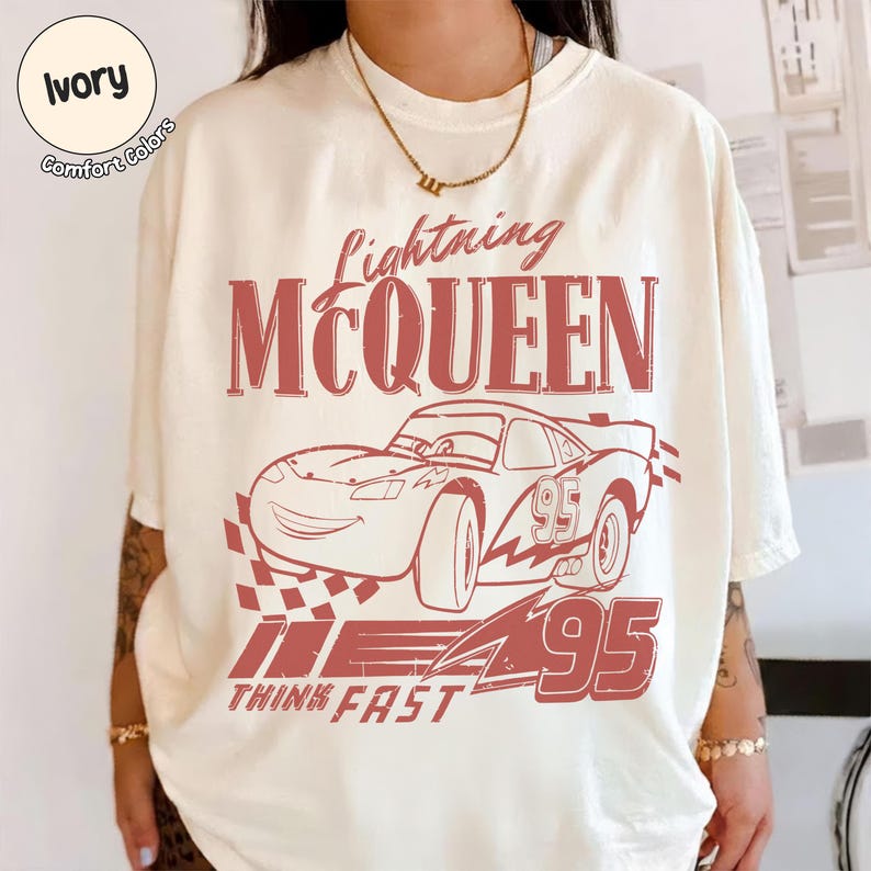 K&ouml;nnte beinhalten: Cremefarbenes T-Shirt mit roter Grafik von Lightning McQueen aus dem Film Cars. Das Design zeigt das Auto, die Nummer 95 und die Worte "Lightning McQueen" und "Think Fast". Das Shirt hat einen Rundhalsausschnitt und kurze &Auml;rmel.