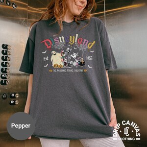 May include: Dark gray t-shirt featuring a colorful "Disneyland" graphic with "Est. 1955" and characters from "The Nightmare Before Christmas". The shirt is a relaxed fit and has short sleeves. The shirt is labeled "Pepper".