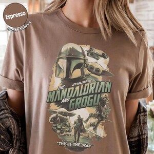 Pu&ograve; includere: T-shirt color espresso con grafica di Star Wars. Il design include The Mandalorian e Grogu, con la frase "THIS IS THE WAY". La maglietta ha le maniche arrotolate e un'etichetta Comfort Colors.