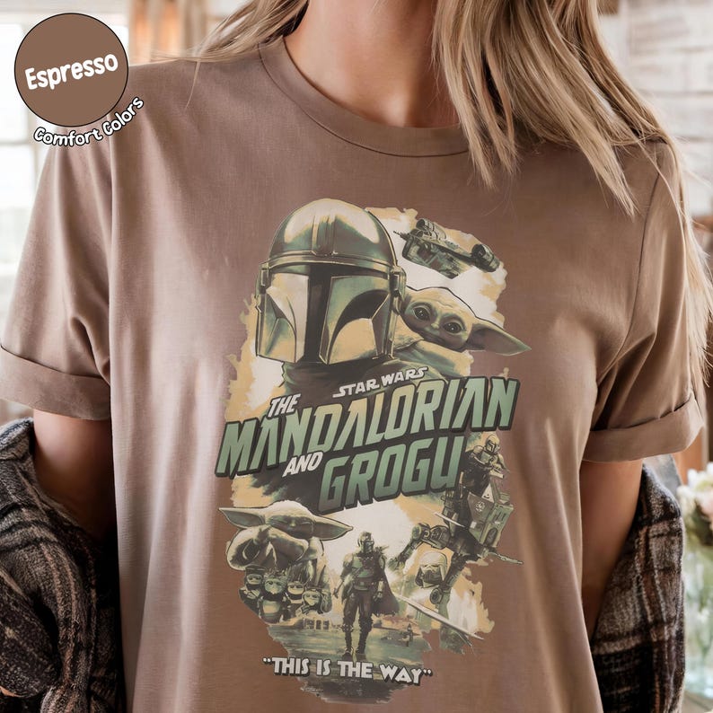 Pu&ograve; includere: T-shirt color espresso con grafica di Star Wars. Il design include The Mandalorian e Grogu, con la frase "THIS IS THE WAY". La maglietta ha le maniche arrotolate e un'etichetta Comfort Colors.