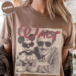 以下が含まれることがあります： エスプレッソ色のTシャツ。ミッキーマウスとウォルト・ディズニーがサングラスをかけているヴィンテージ風グラフィックと、赤いスクリプトフォントで「Walt」の文字がプリントされています。Comfort Colorsブランドのシャツです。