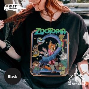 May include: Black crew neck t-shirt featuring a colorful graphic from the animated movie Zootopia. The design includes the movie title and various characters. The shirt has a vintage, retro style.