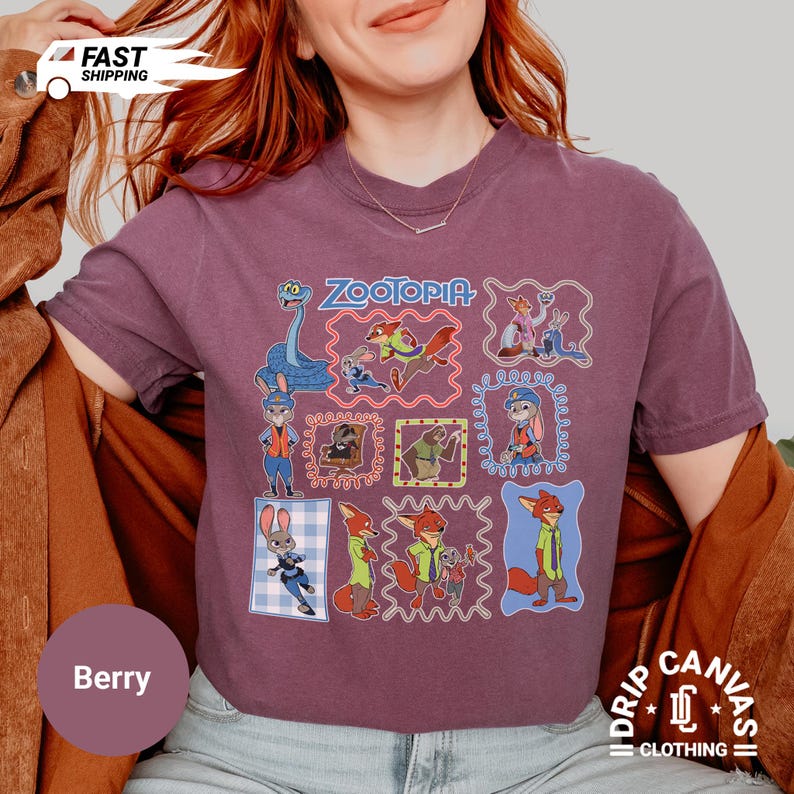 May include: Berry-colored t-shirt featuring a colorful Zootopia design. The design includes various characters from the movie, framed in decorative borders. The shirt has a crew neck and short sleeves. The text "Zootopia" is printed at the top.