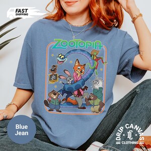 May include: Blue jean colored t-shirt featuring the word "Zootopia" above a graphic of characters from the animated movie. The shirt has a crew neck and short sleeves. The shirt is made of a soft, comfortable material.