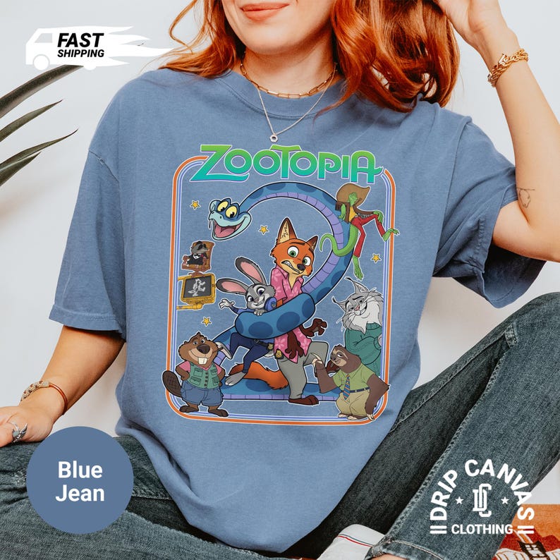 May include: Blue jean colored t-shirt featuring the word "Zootopia" above a graphic of characters from the animated movie. The shirt has a crew neck and short sleeves. The shirt is made of a soft, comfortable material.