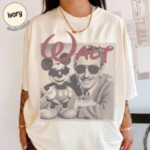 以下が含まれることがあります： アイボリー色のTシャツ。ミッキーマウスとウォルト・ディズニーがサングラスをかけているヴィンテージスタイルのグラフィックが特徴で、"Walt"の文字はバーガンディ色。シャツには"Comfort Colors"とプリントされています。