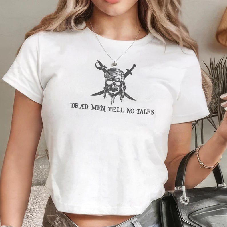 May include: White t-shirt featuring a black pirate skull graphic with crossed swords and the text "DEAD MEN TELL NO TALES". The design is centered on the front of the short-sleeved shirt.