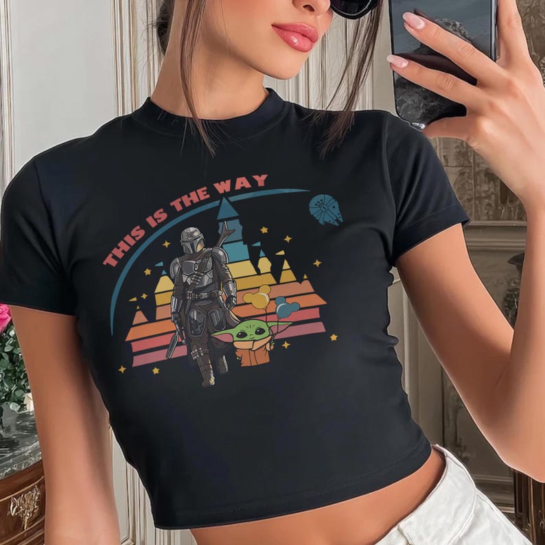 May include: Black crop top featuring a colorful graphic of The Mandalorian and Grogu, with the text "THIS IS THE WAY" in pink. The design includes a sunset-colored background with stars and a spaceship.