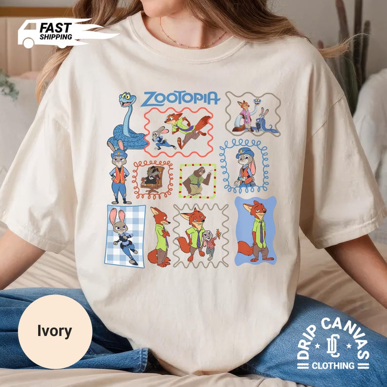 May include: Ivory-colored t-shirt featuring colorful cartoon illustrations of characters from the movie "Zootopia." The shirt includes the movie title and various character portraits within decorative frames. The shirt is part of the "Drip Canvas Clothing" collection.
