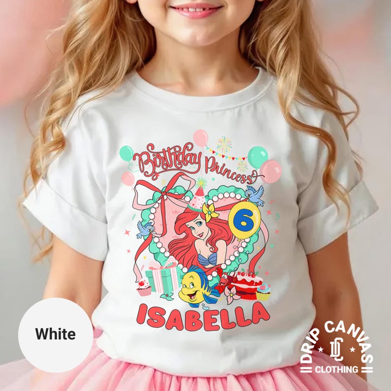 May include: White t-shirt featuring a colorful graphic of a princess with red hair, a blue top, and the number 6. The shirt includes the text "Birthday Princess" and the name "Isabella".