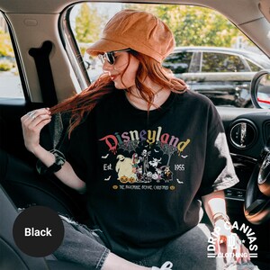 May include: Black t-shirt with a Disneyland graphic featuring characters from The Nightmare Before Christmas. The design includes the text "Disneyland Est. 1955" in a colorful, dripping font, with spiderwebs and bats. The shirt is part of the Drip Canvas Clothing collection.