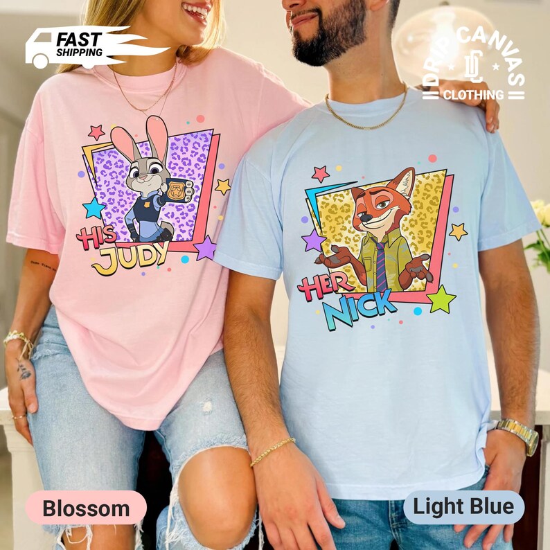 May include: Two t-shirts, one blossom pink and one light blue, featuring cartoon characters. The pink shirt has a Judy Hopps graphic with "HIS JUDY" text. The blue shirt has a Nick Wilde graphic with "HER NICK" text. Both shirts have a crew neck.