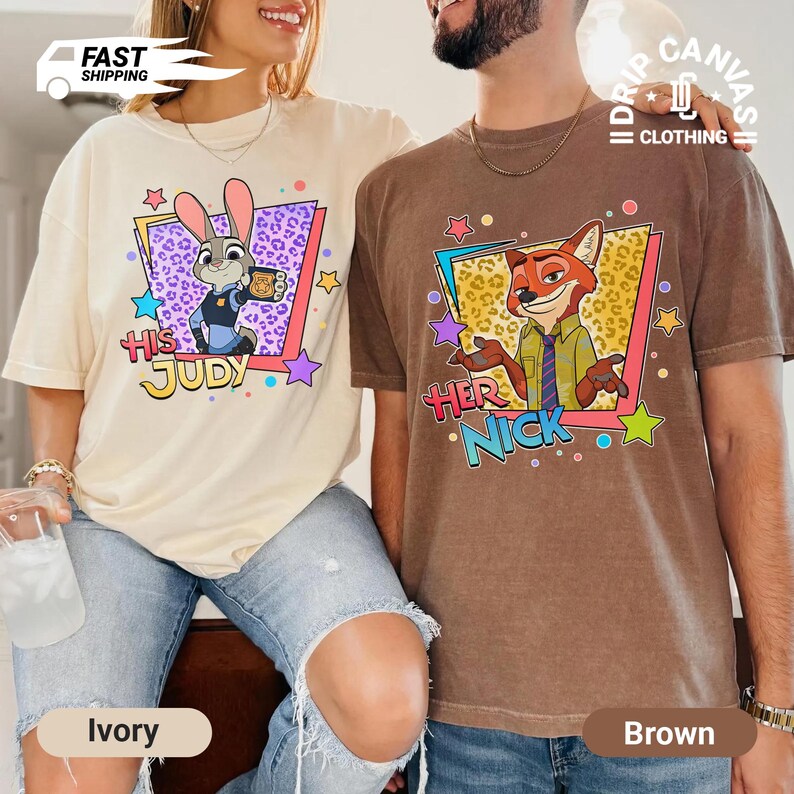 May include: Ivory and brown t-shirts featuring cartoon characters from Zootopia. The ivory shirt has Judy Hopps with the text "His Judy", while the brown shirt has Nick Wilde with the text "Her Nick". Both shirts have a colorful design.