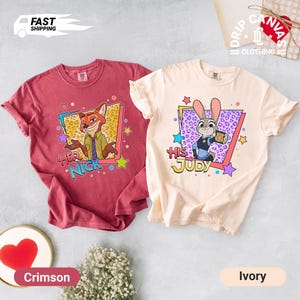 May include: Two Zootopia-themed t-shirts. One crimson shirt features Nick Wilde with "Her Nick" text. The other is ivory with Judy Hopps and "His Judy" text. Both shirts have colorful star and geometric designs.