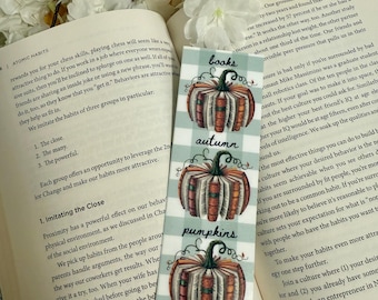 May include: A decorative bookmark featuring three pumpkin illustrations made of books, with the words "books", "autumn", and "pumpkins" in a whimsical font. The bookmark has a light blue and white checkered pattern.