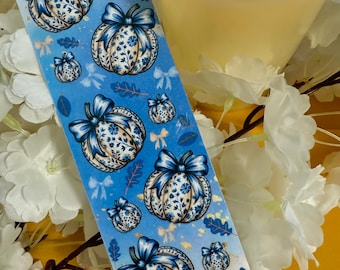 Puede incluir: Un rollo de cinta adhesiva decorativa azul con un patrón repetido de calabazas con lazos azules y diseños florales. Las calabazas tienen un patrón floral blanco y azul. El fondo es azul claro con pequeños lazos y hojas.
