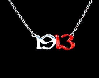 Op de afbeelding: Een zilveren ketting met een hanger met de nummers "19" in zilver en "13" in rood.