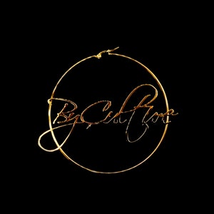 May include: A gold-colored hoop earring with the cursive text "By Celina Rose" inside the hoop. The earring is set against a black background, highlighting the jewelry's design and color.
