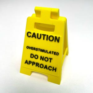 Señal de precaución sobreestimulación para escritorio: amarilla con texto negro, mensaje de advertencia para concienciar sobre la seguridad.