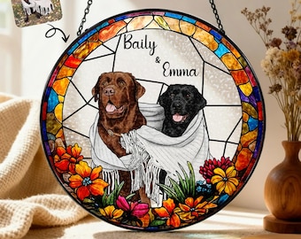 May include: A round, stained-glass window featuring a brown and black Labrador Retriever, wrapped in a white blanket. The names "Baily & Emma" are above the dogs. The window is decorated with colorful flowers and a stained-glass border.