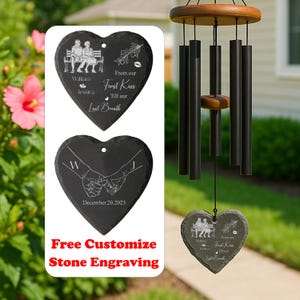 May include: A heart-shaped wind chime with a wooden top and black chimes. The wind chime has a heart-shaped stone pendant with engraved text and illustrations. The text reads "William & Jessica", "First Kiss Till our Last Breath", and "December.20.2023".