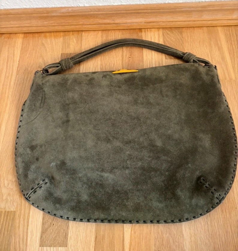 May include: Olive green suede handbag with a rounded shape and a top handle. The bag features a contrasting yellow accent and decorative stitching around the edges. The handle is knotted at the top.