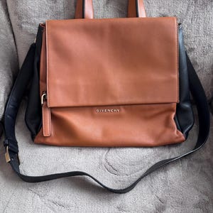 May include: A brown and black leather handbag with a top handle and a shoulder strap. The bag has a flap closure and the word "GIVENCHY" is embossed on the front.