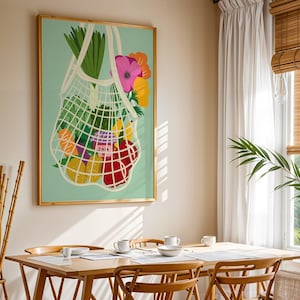 May include: A framed art print shows a white mesh bag filled with colourful fruits, vegetables, and flowers against a light teal background. The print is in a gold frame and hangs above a wooden dining table with place settings.