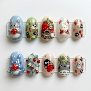 K&ouml;nnte beinhalten: Ein Set aus zehn k&uuml;nstlichen N&auml;geln mit verschiedenen Designs. Die Designs umfassen Zeichentrickfiguren, Erdbeeren, Blumen und Glitzer. Die N&auml;gel sind in verschiedenen Farben gehalten, darunter Blau, Gr&uuml;n, Rot und Rosa. Die N&auml;gel sind oval geformt.
