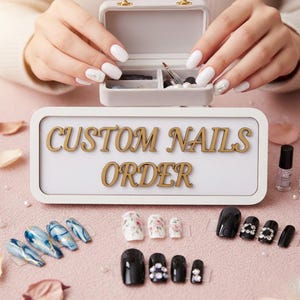 May include: A display of custom nail designs, including blue marble, floral, and solid black styles. The image features a sign that reads "CUSTOM NAILS ORDER" and a small case with nail tools. A bottle of nail polish is also visible.
