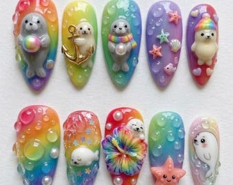 May include: A set of ten artificial nails with a variety of colorful designs. Each nail features a different design, including seals, anchors, starfish, and floral elements. The nails are painted in a rainbow of colors, with a glossy finish.