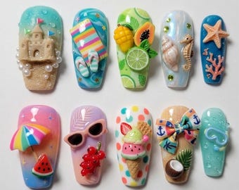 Puede incluir: Una colección de diseños de uñas con temática veraniega. Cada uña presenta adornos 3D únicos, incluyendo un castillo de arena, una toalla de playa, frutas, conchas marinas y conos de helado. Las uñas muestran una variedad de colores y texturas.