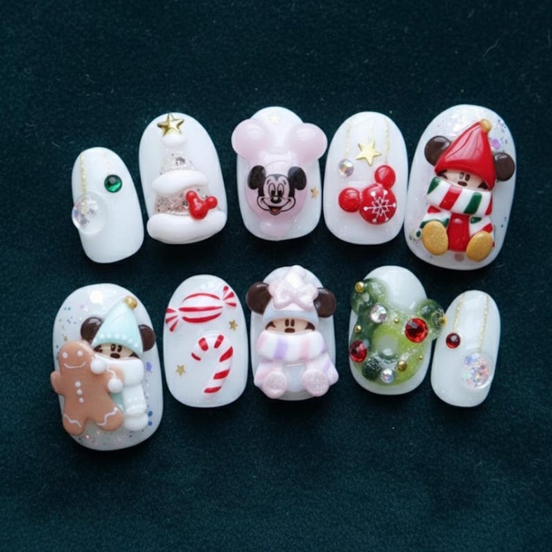May include: A set of ten white acrylic nails with various Christmas-themed designs. The designs include a Christmas tree, Mickey Mouse, a gingerbread man, candy canes, and a snowman. Some nails feature glitter and 3D embellishments.