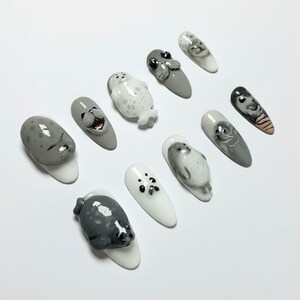 Puede incluir: Una colecci&oacute;n de diez u&ntilde;as artificiales, cada una con un dise&ntilde;o &uacute;nico de foca en 3D. Las u&ntilde;as presentan una variedad de colores, incluyendo blanco, gris y negro, con caras y cuerpos de foca detallados. El arte de u&ntilde;as muestra un tema l&uacute;dico y art&iacute;stico.