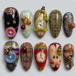 May include: A set of ten decorative nail art tips featuring 3D elements including a black cat with a pink button, ladybugs on a daisy, a clock with a worm, plaid patterns with water droplets, a snail, a bee with a blue button, and a fruit clock.