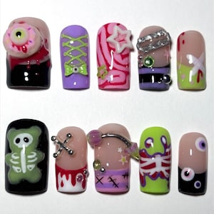 May include: A set of ten press-on nails featuring diverse designs including a 3D eyeball, a green skeleton bear, corset lacing, pink swirls, silver accents, red blood drips, stitches, and neon green patterns in a mix of black, pink, purple, and lime.
