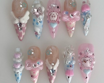 May include: A set of ten long, pointed artificial nails. Each nail features a unique design with pink, blue, and white accents. Decorations include bows, hearts, wings, and cartoon characters, with glitter and rhinestones.