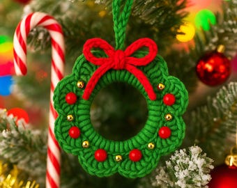 May include: A handmade green crochet Christmas wreath ornament with a red bow and red bead accents. The wreath is hanging on a Christmas tree with a candy cane and red ornaments in the background.