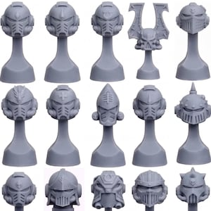 May include: A collection of gray miniature helmet models, each mounted on a slender pedestal. The helmets showcase various designs, including visors, crests, and intricate detailing, suggesting a science fiction or fantasy theme. The models are arranged in neat rows.