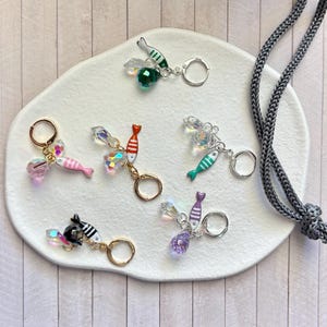May include: A collection of colorful fish-shaped keychains. Each keychain features a small, detailed fish design with various colors, including pink, red, green, and purple, accented with clear crystal beads. The keychains have silver and gold-toned rings.